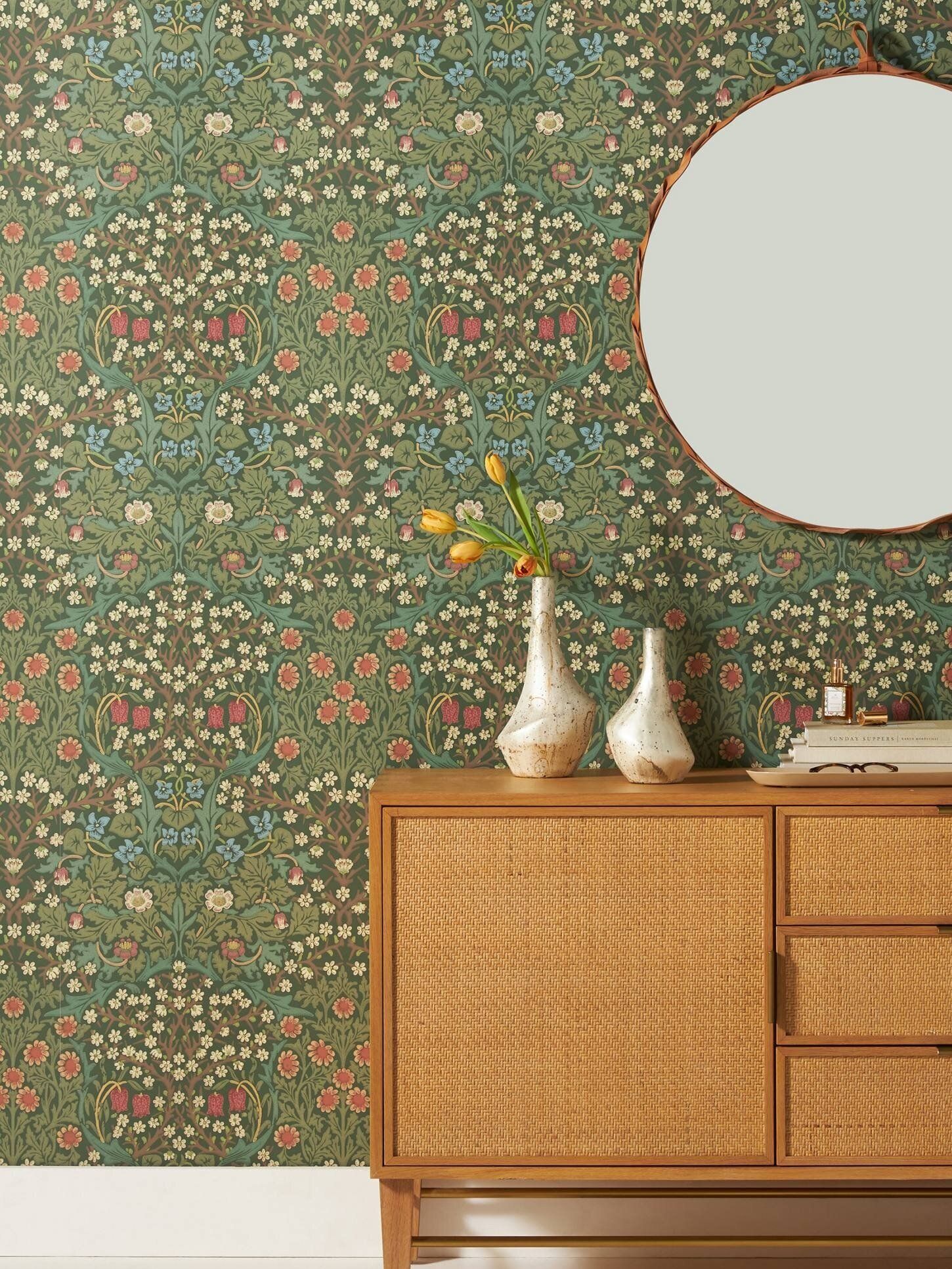 Floral wallpaper as backdrop for circular wall mirror and credenza with vases and details.