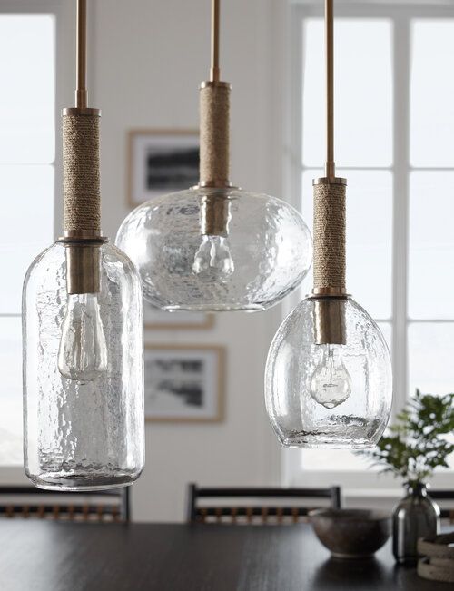 Three glass pendants in different shapes with a "hammered" texture hanging over a dining table.