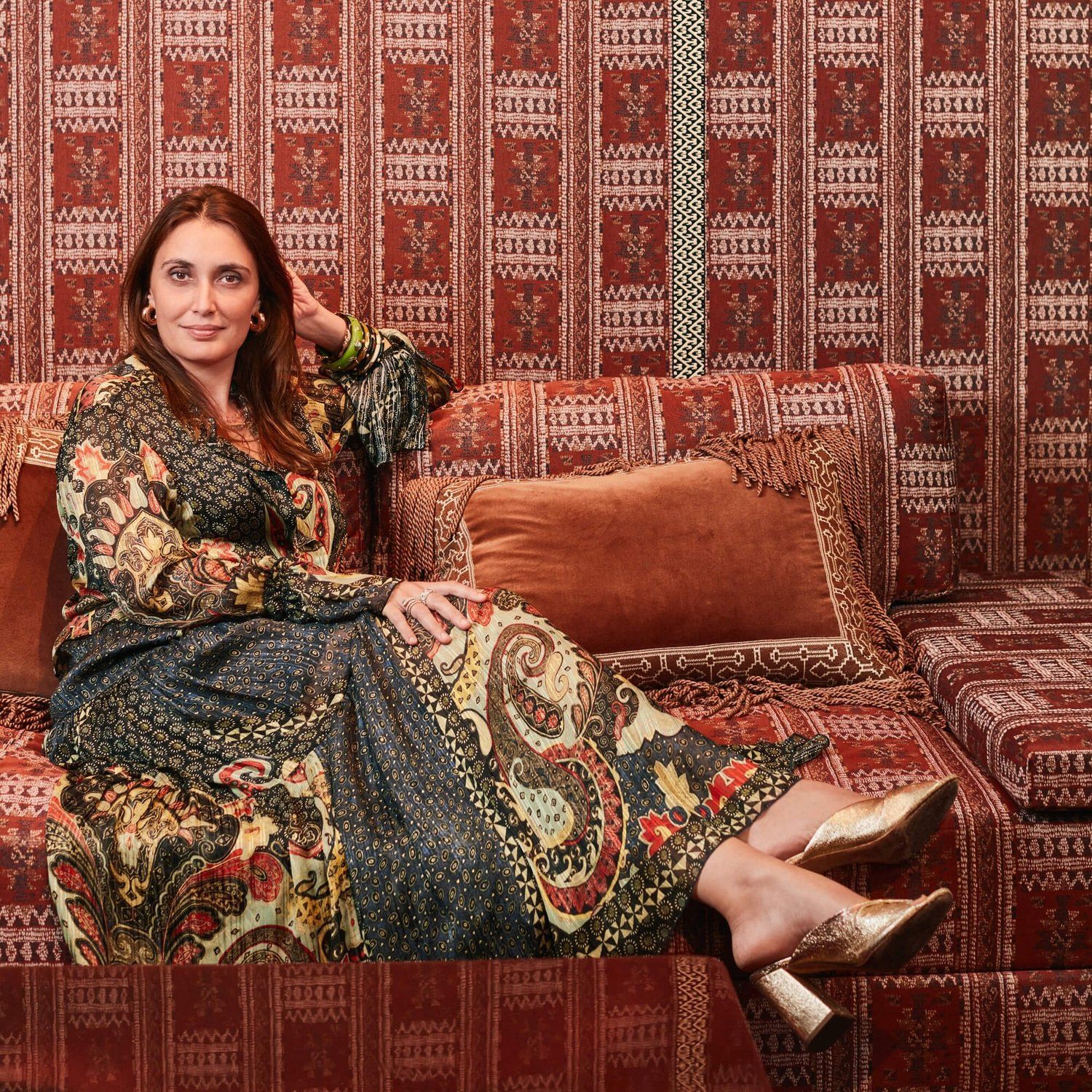 Stylish woman draped on couch that is upholstered in same pattern as wallcovering.
