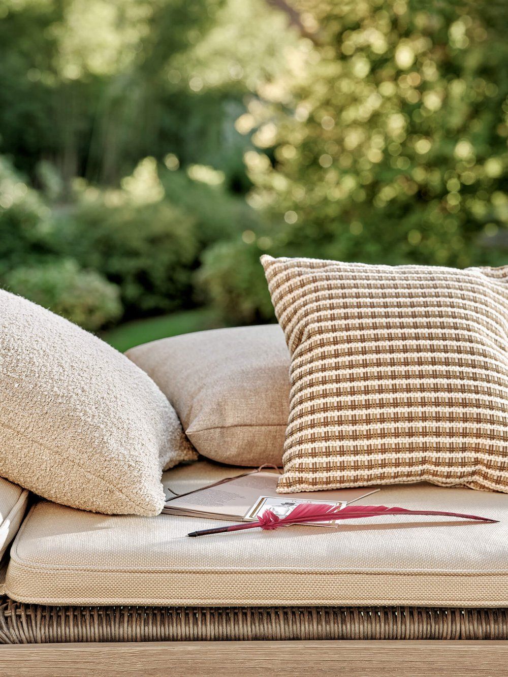Upholstered pad on a wicker lounge with a group of coordinated pillows setting on it.