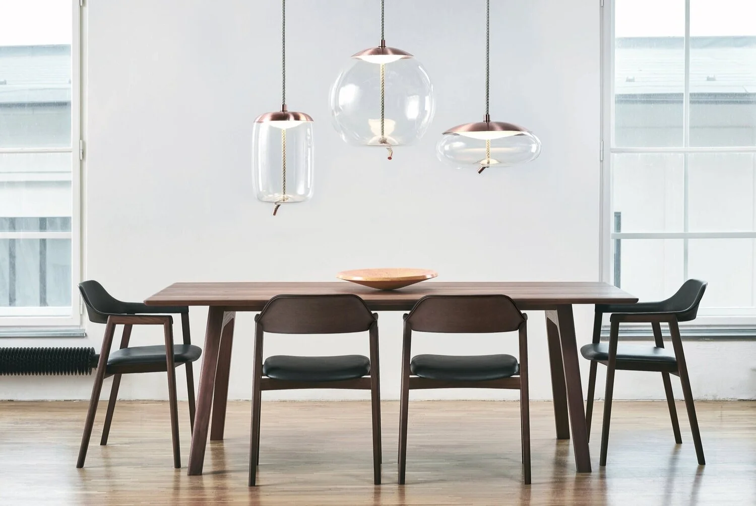 Modern dining room table and chairs with 3 pendant lights hanging above.