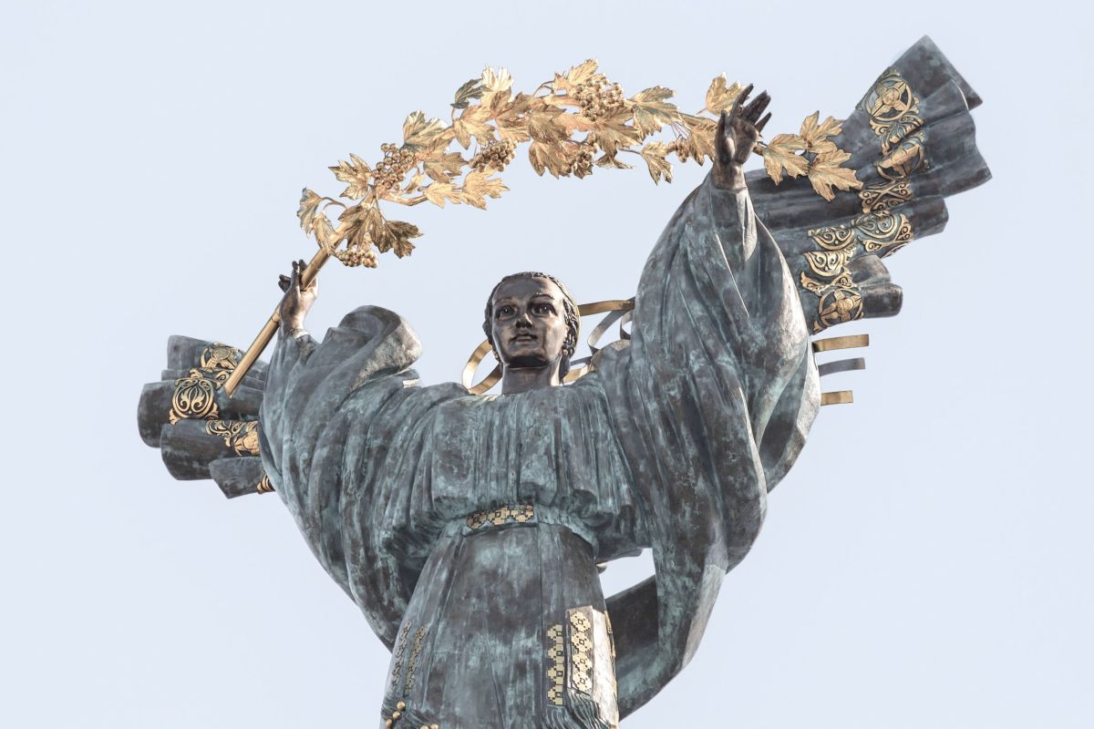A statue of a woman with a bough of golden leaves over her.