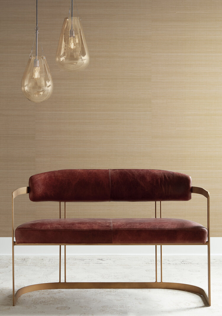 Modern loveseat with curved metal frames and upholstered back and seat with two pendulum lamps above and a grasscloth covered wall behind.