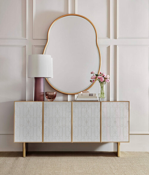 A curvy mirror with gold colored frame over credenza with similar trim.
