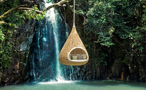 Lounge chair shaped like a seed pod hanging above a waterfall fed pool.