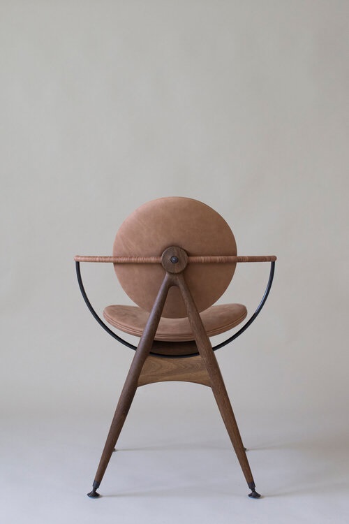 Chair with curved back metal arms, round back and seating pillows. From behind it looks like a drawing compass.