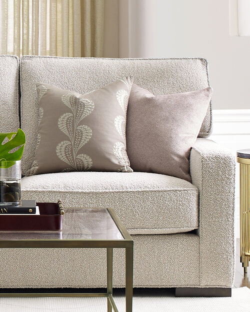 Upholstered contemporary couch with pillows behind a glass and brass coffee table.