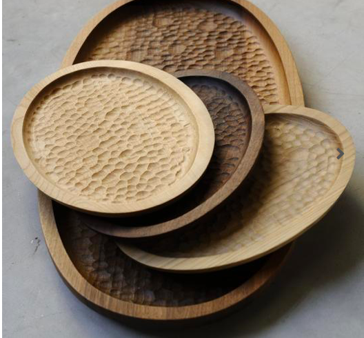 A stack of carved trays in different shapes with textured interior bottoms.