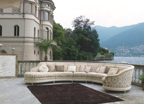 Large formal curved couch on a balcony overlooking European waterfront.