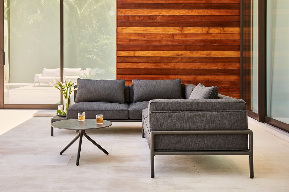 Metal and upholstered L-shaped couch with small round coffee table outside a modern home.