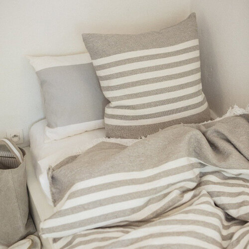 Striped natural color woven pillow and blanket on a twin bed.