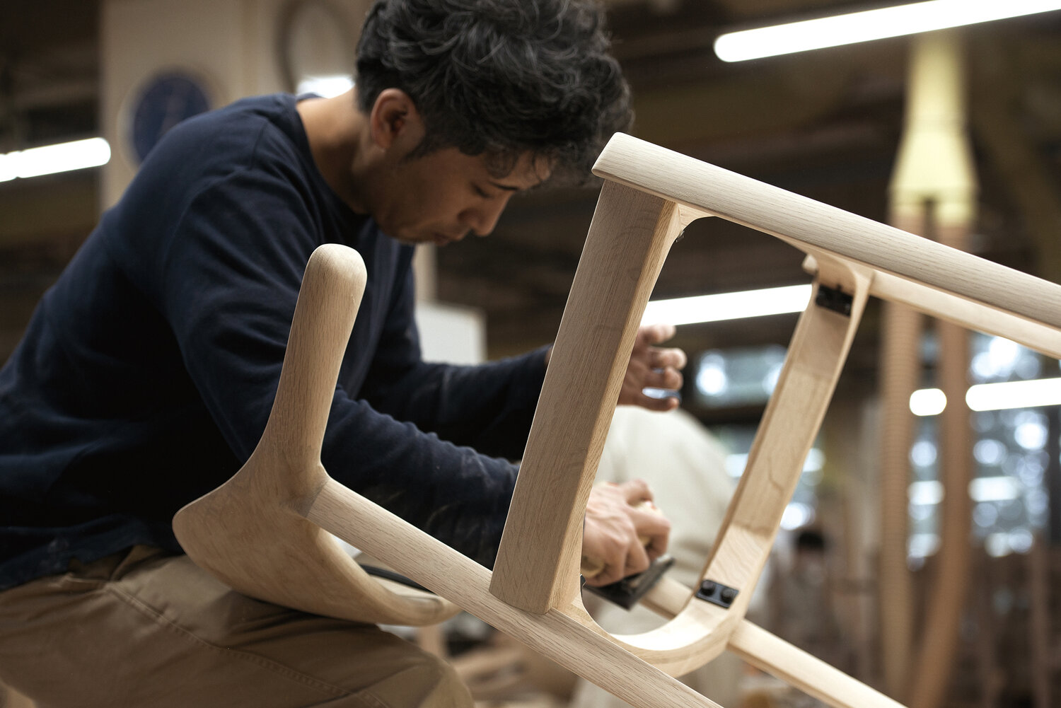 Man sanding the wood frame of a chair.
