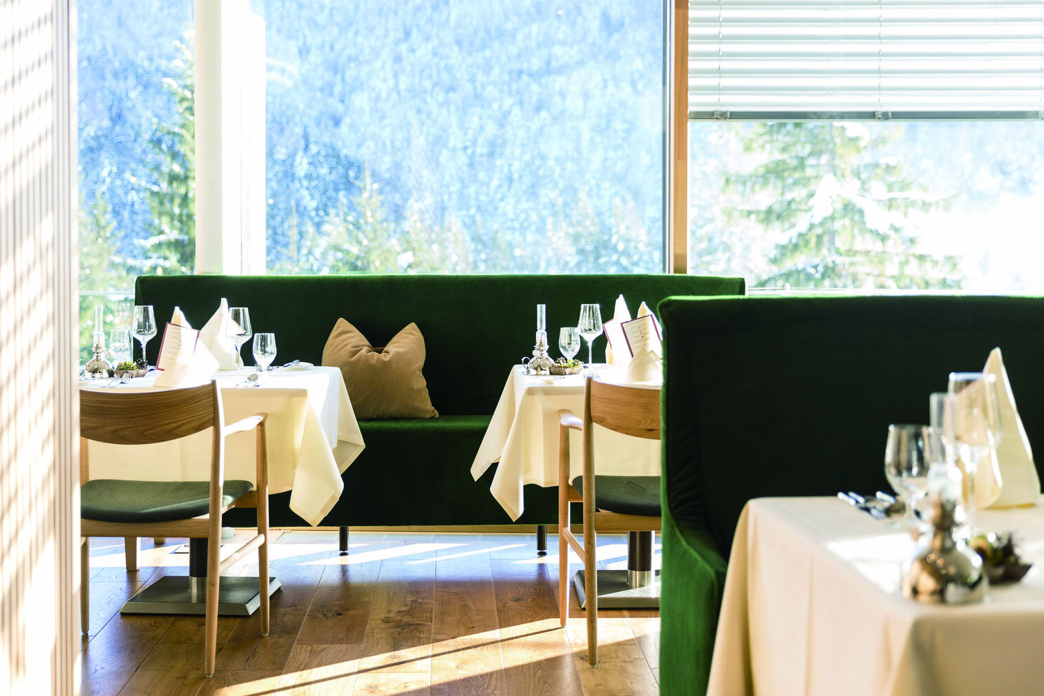 Modern restaurant dining room set for service with banquette seating in front of floor to ceiling glass overlooking the mountains.