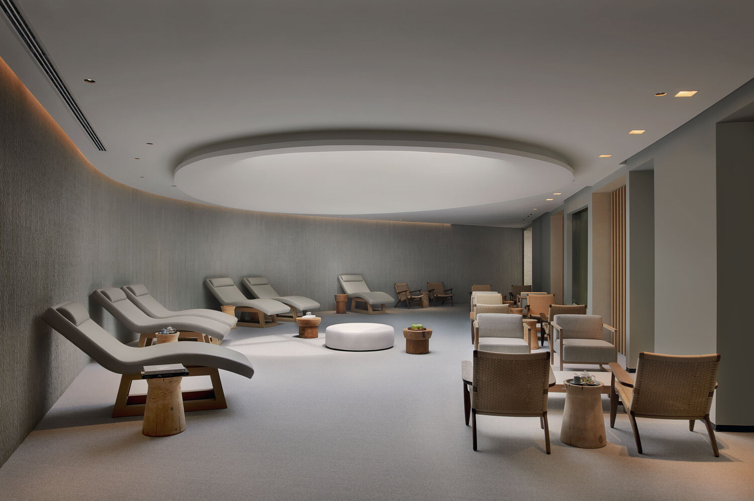 Monotone modern room with row of lounge chairs along a curved wall and small seating areas to the right.