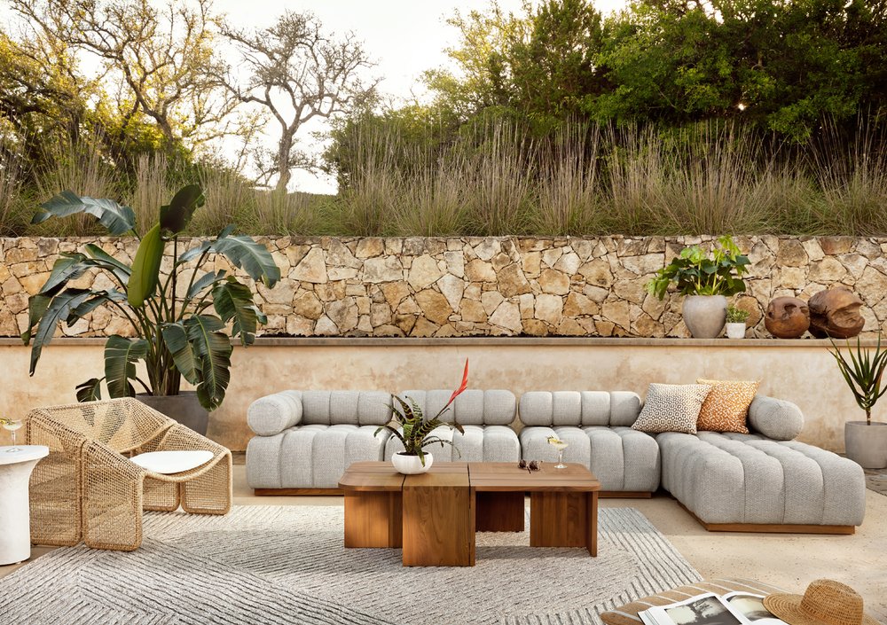 Channel upholstered outdoor couch and lounge with woven chairs, wooden cocktail table in front of a garden wall.