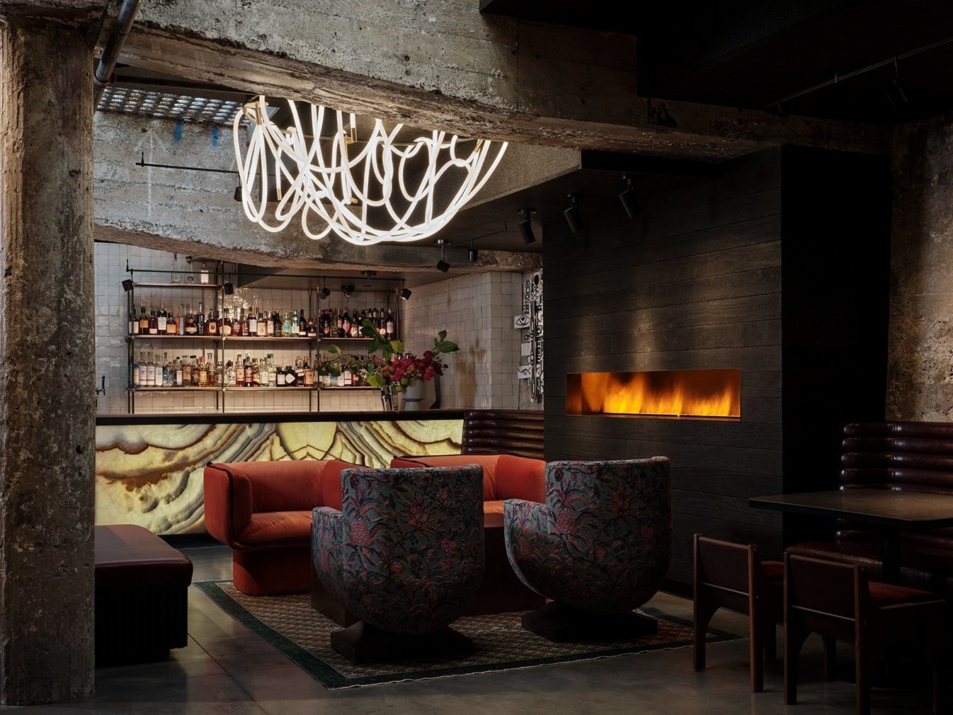 Cozy seating area in foreground, with a large modern gas fireplace on right and a bar in center background.