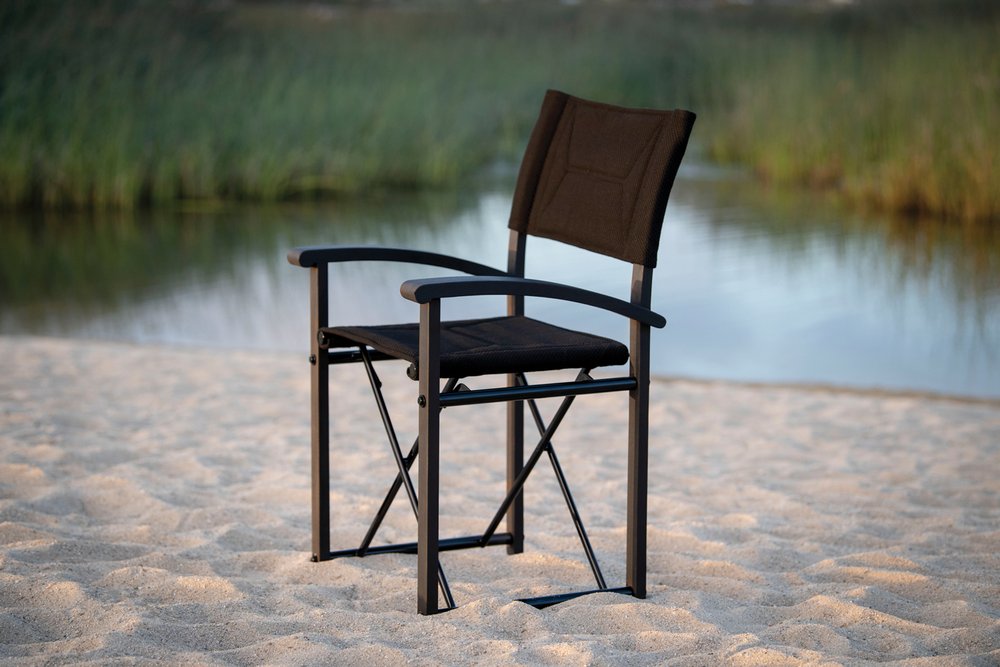 Simple director's style chair on sand next to small lake.